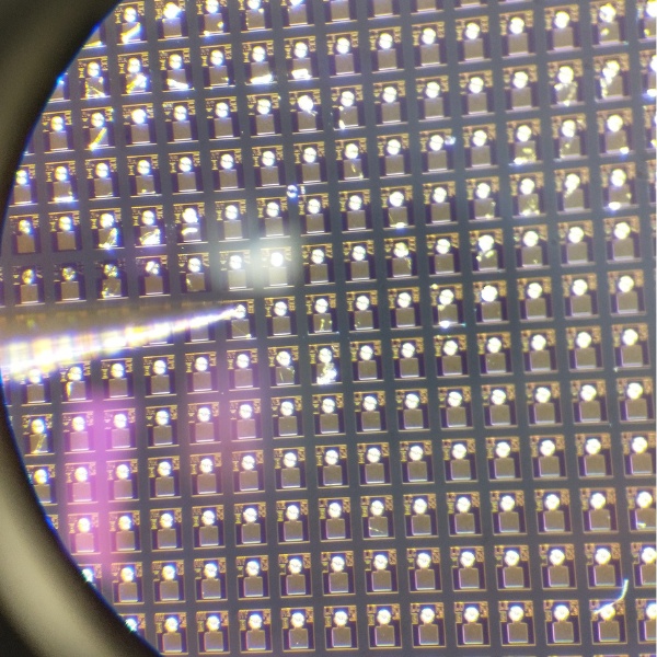 A VCSEL wafer seen through a microscope, showing hundreds of individual dies across its surface.